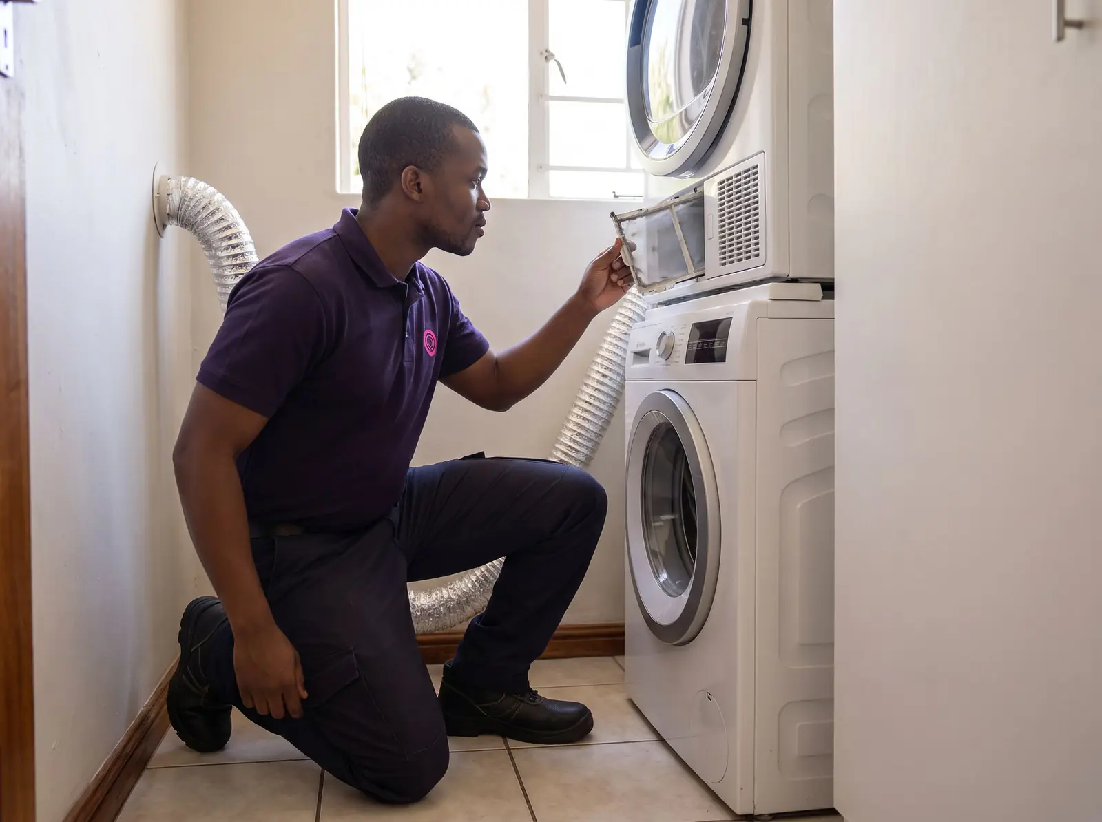 A technician pulls the lint filter from a tumble dryer stacked on a washing machine
